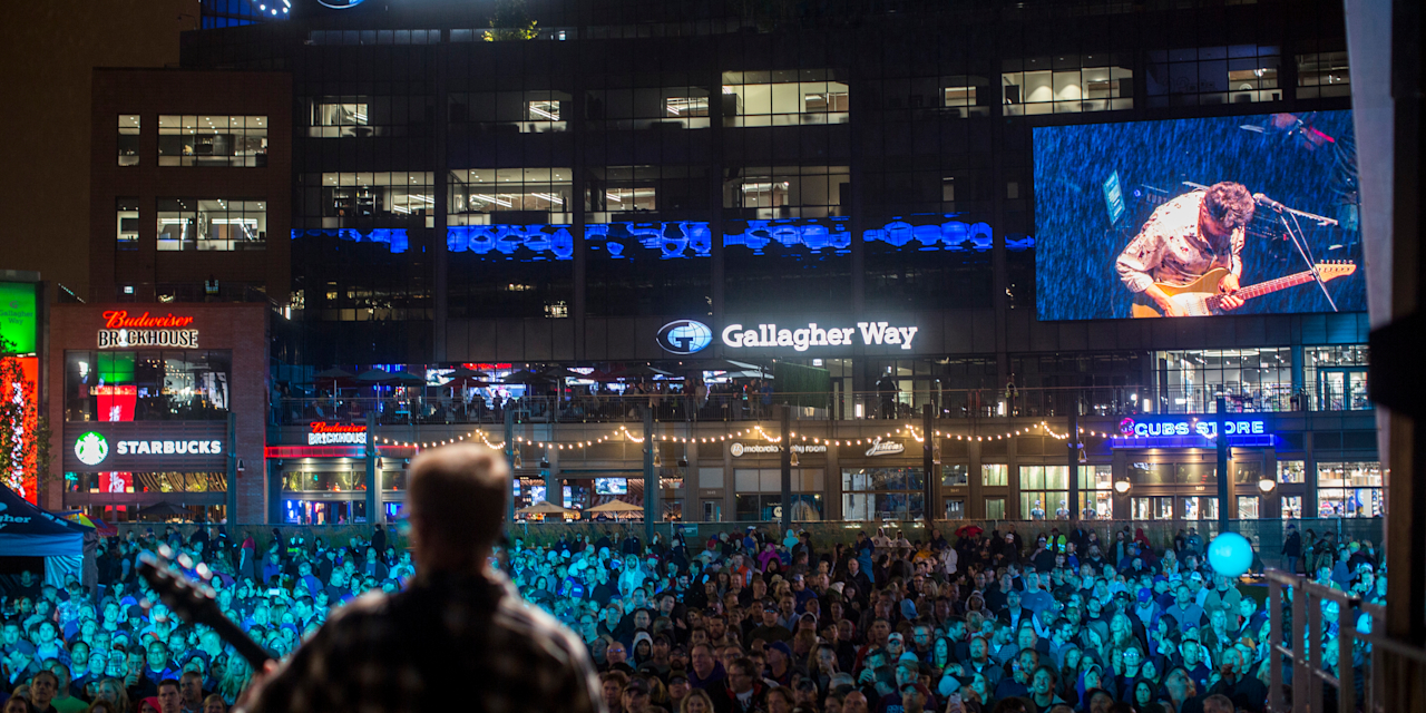 Nighttime concert crowd on the Gallagher Way lawn with the stage lit up in front of the plaza
